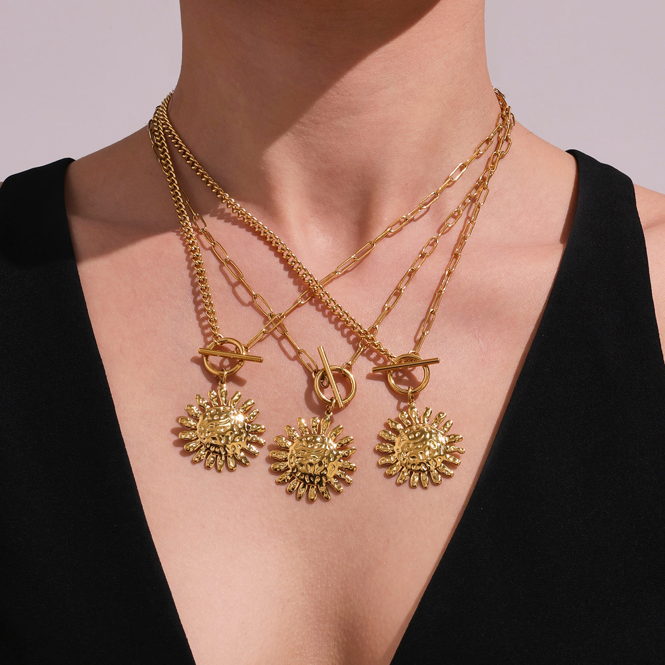 Gold necklaces with floral pendants on a person wearing a black top.