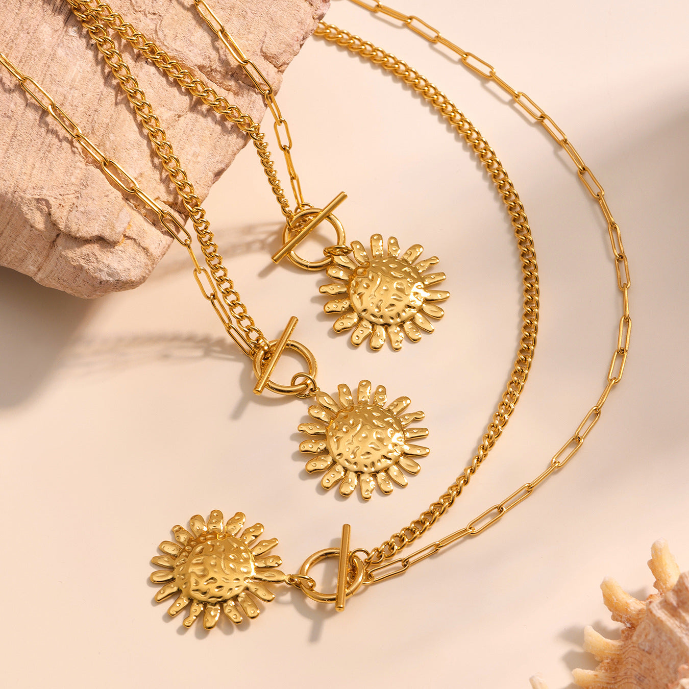 Gold necklaces with sunflower pendants on a beige background