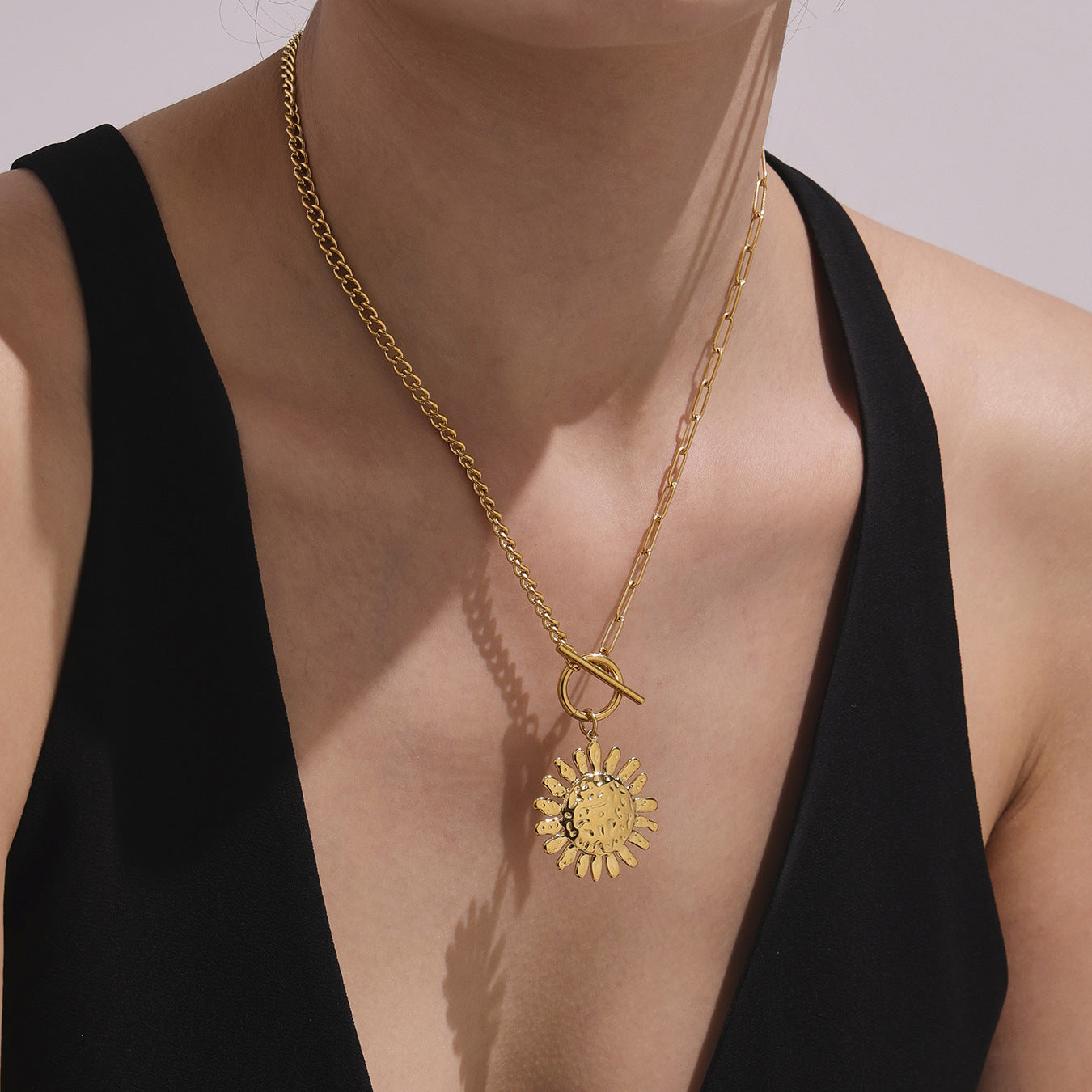 Gold necklace with a sunflower pendant worn by a person in a black top.