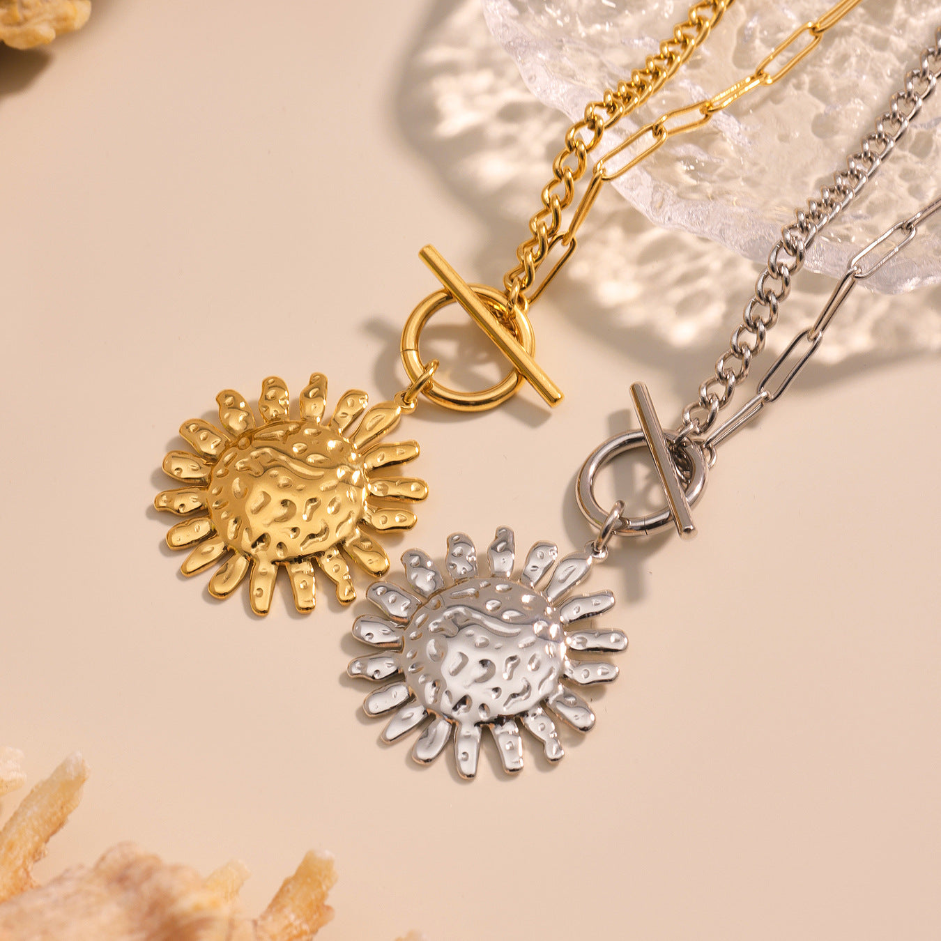 Two sun-shaped pendants on gold and silver chains against a beige background