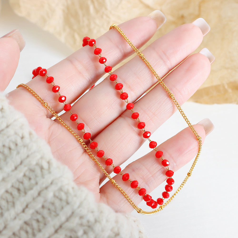 Hand wearing a gold chain with red beads on a neutral background