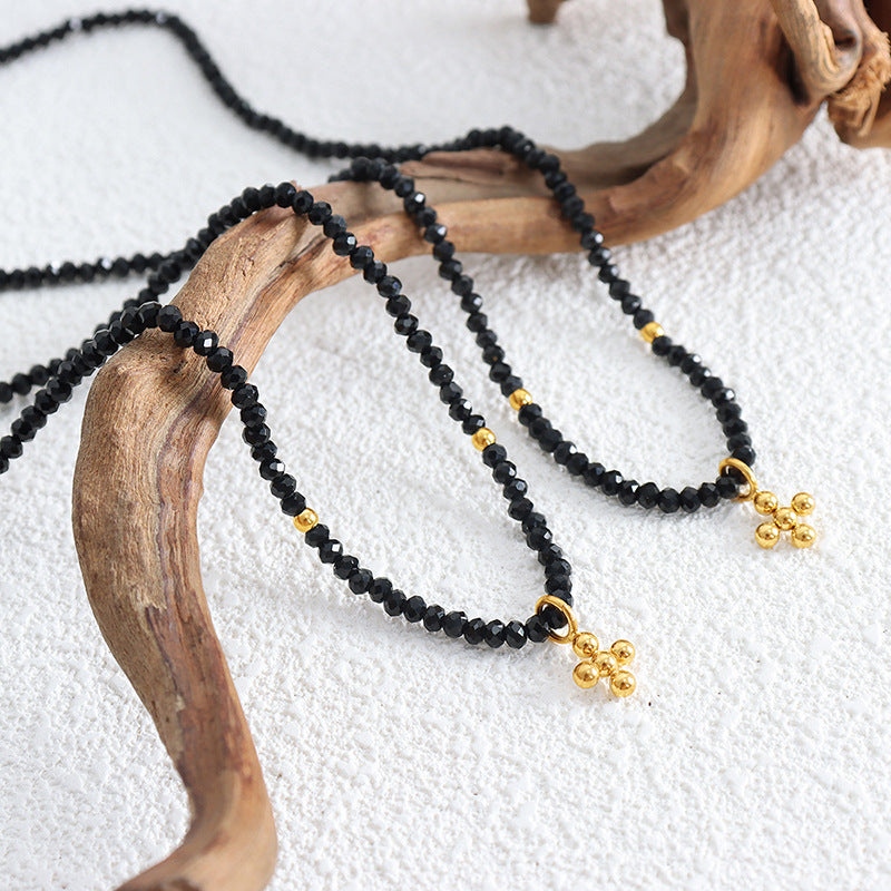 Black beaded necklace with gold accents on a white surface with wooden branch