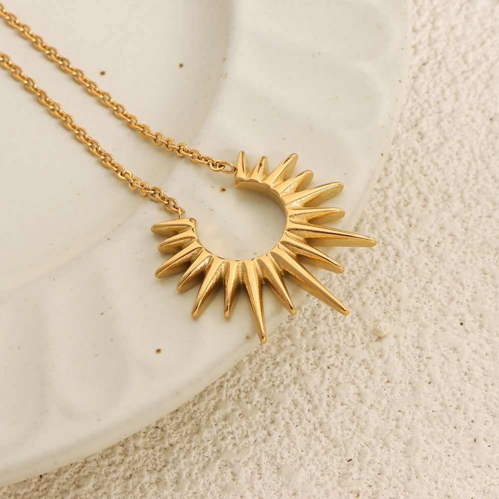 Gold sun-shaped pendant necklace on a textured beige surface