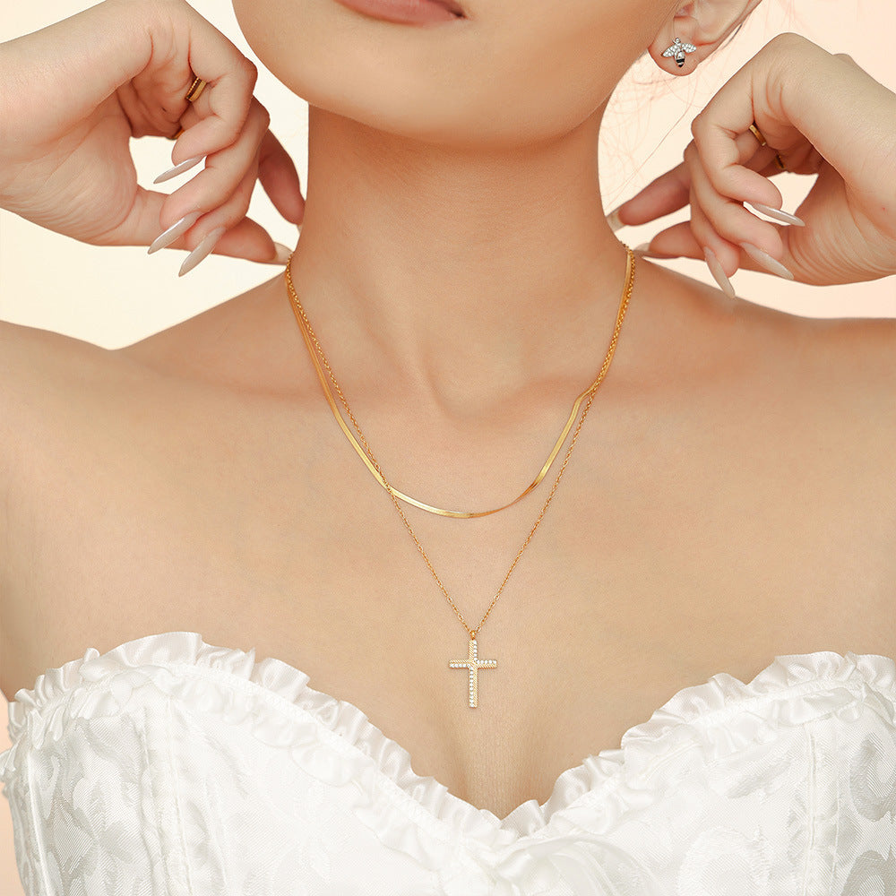 Gold necklace with a cross pendant worn by a person, with hands adjusting the jewelry against a light background.
