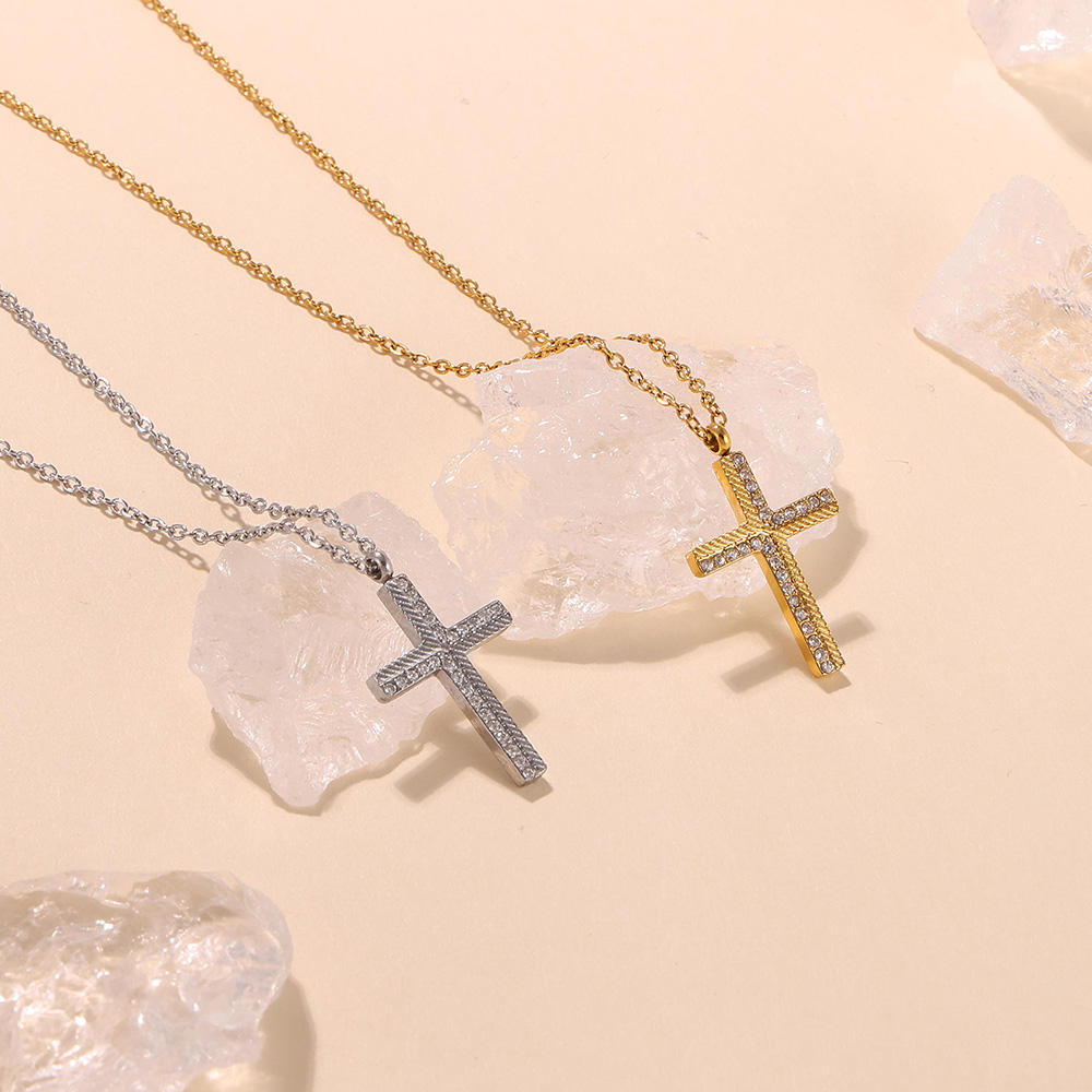 Two cross-shaped necklaces, one gold and one silver, on a beige background with crystal stones.