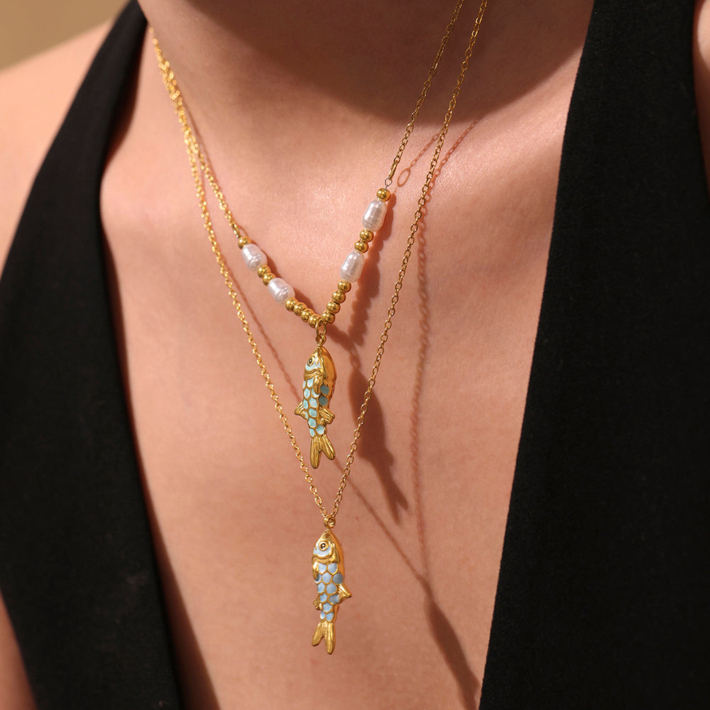 Gold fish-shaped necklace with gemstones on a person wearing a black top.