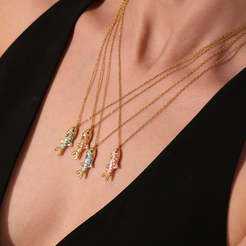 Gold necklaces with fish pendants on a person wearing a black top.