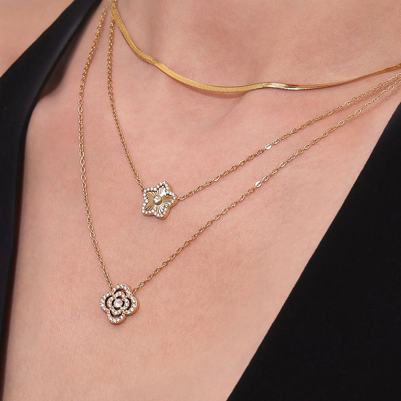 Two gold necklaces with floral pendants on a person wearing a black top.