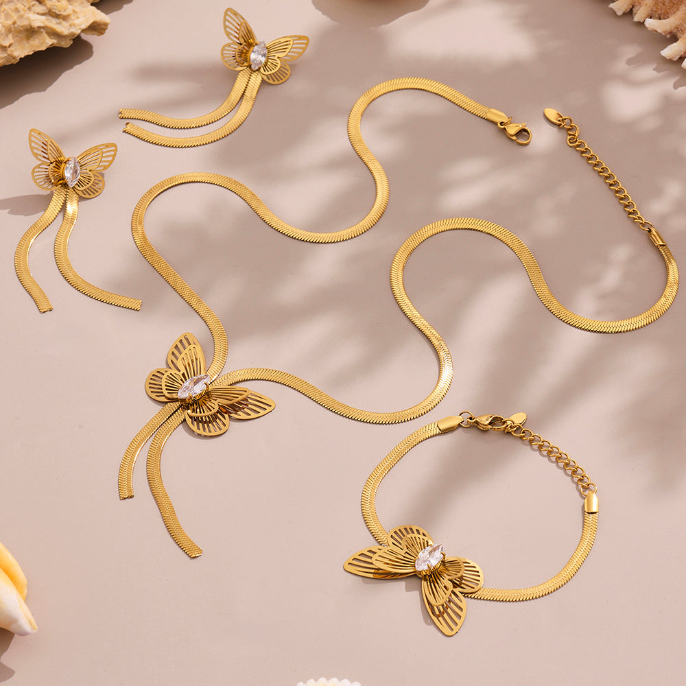 Gold butterfly necklace and bracelet set on a beige surface with natural light shadows.