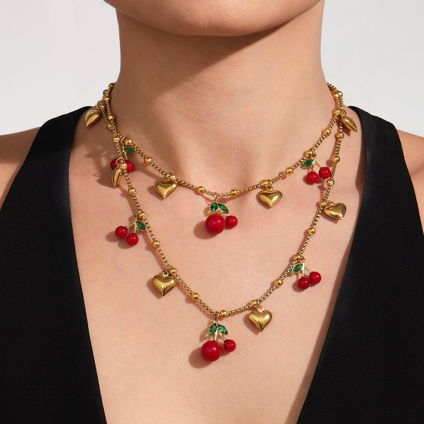 Gold necklace with red berry and heart charms on a plain background