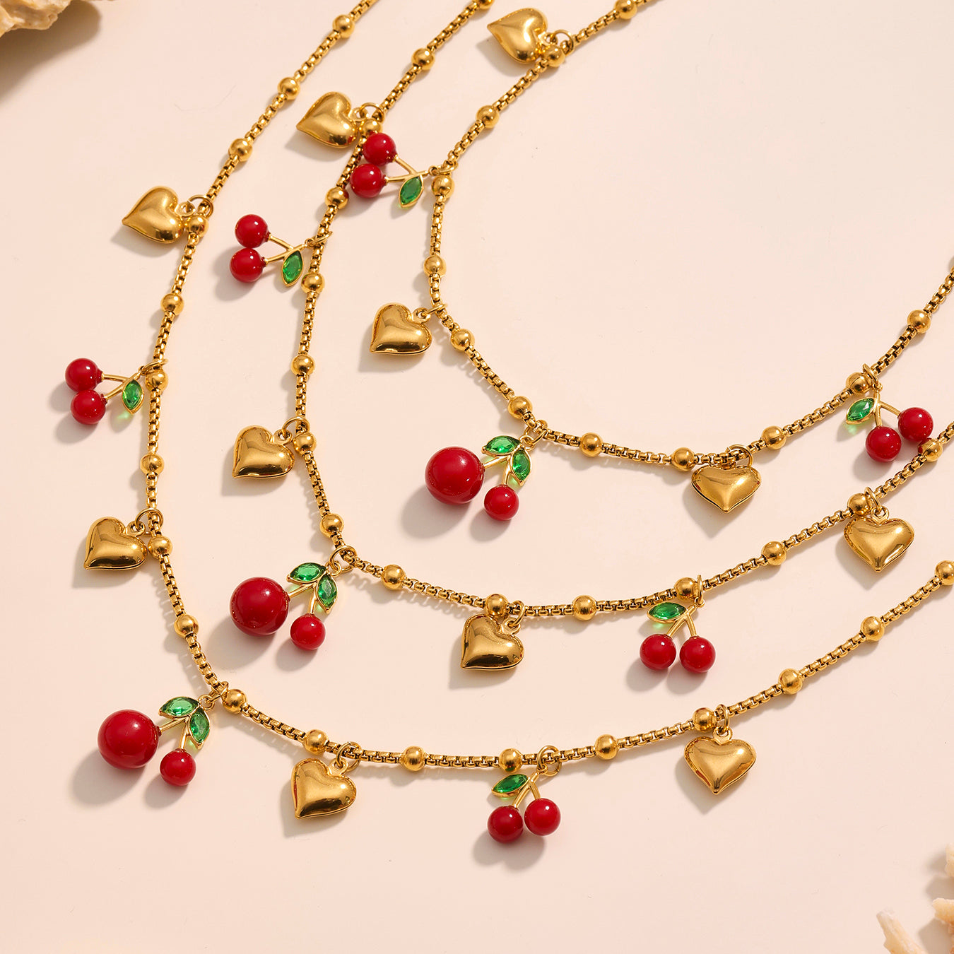 Gold necklaces with heart and cherry pendants on a beige background