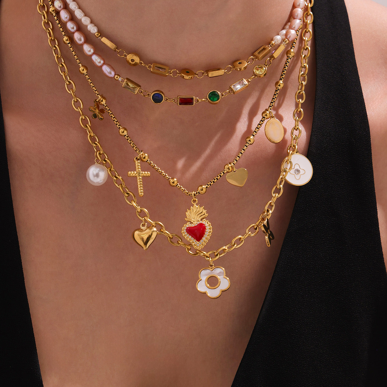 Multiple gold necklaces with various charms on a person wearing a black top.