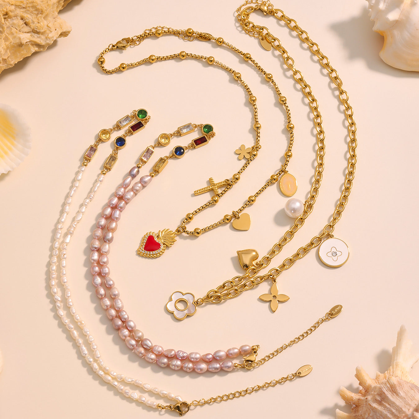 Gold necklaces with various charms on a beige surface with seashells.
