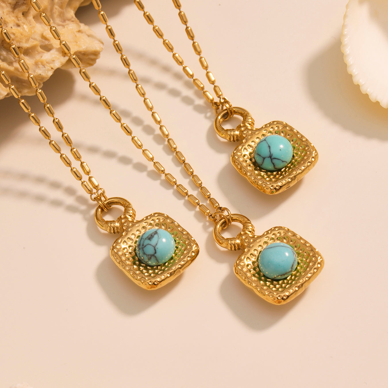 Gold necklaces with turquoise stones on a beige surface