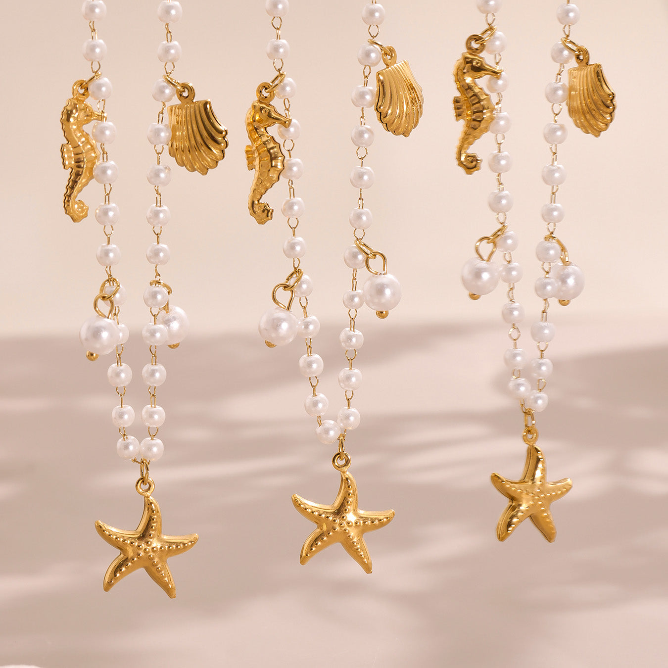 Pearl necklaces with gold seahorse, shell, and starfish charms on a beige background