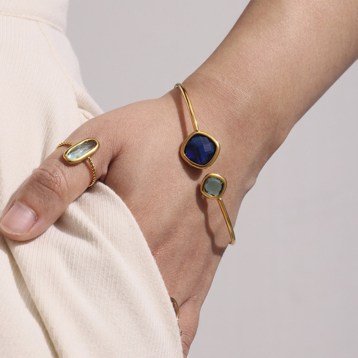 Gold bracelet with a blue gemstone worn on a wrist against a neutral background