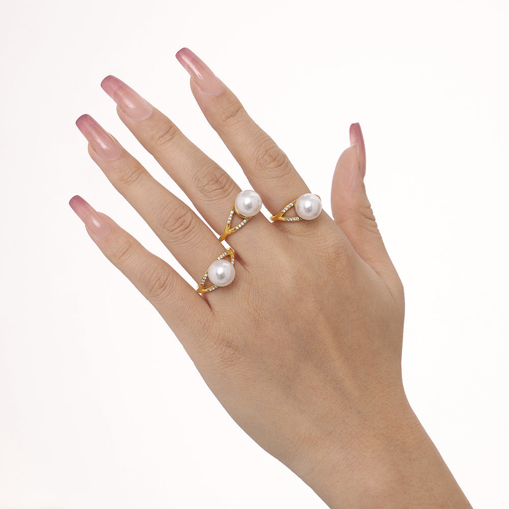 Close-up of a hand wearing a pearl-accented gold ring on a white surface