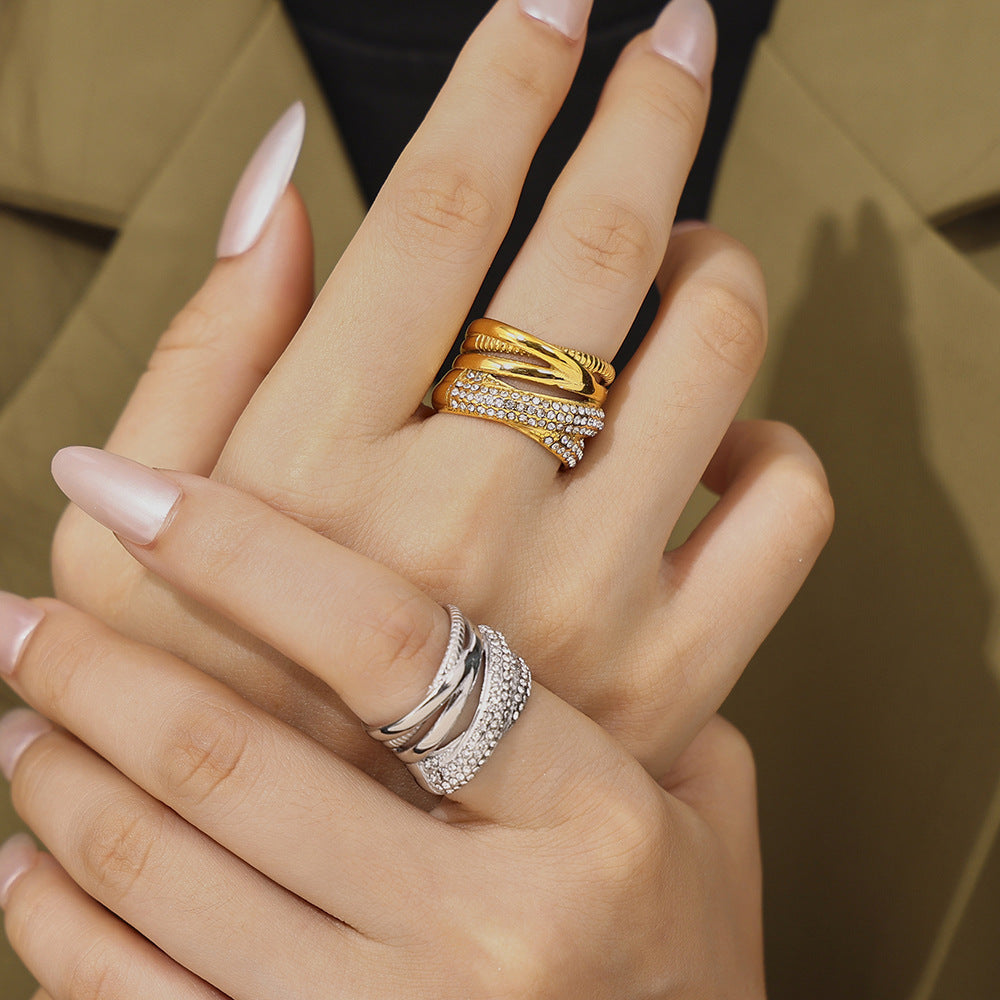 Hand wearing two rings with gold and silver bands on a neutral background