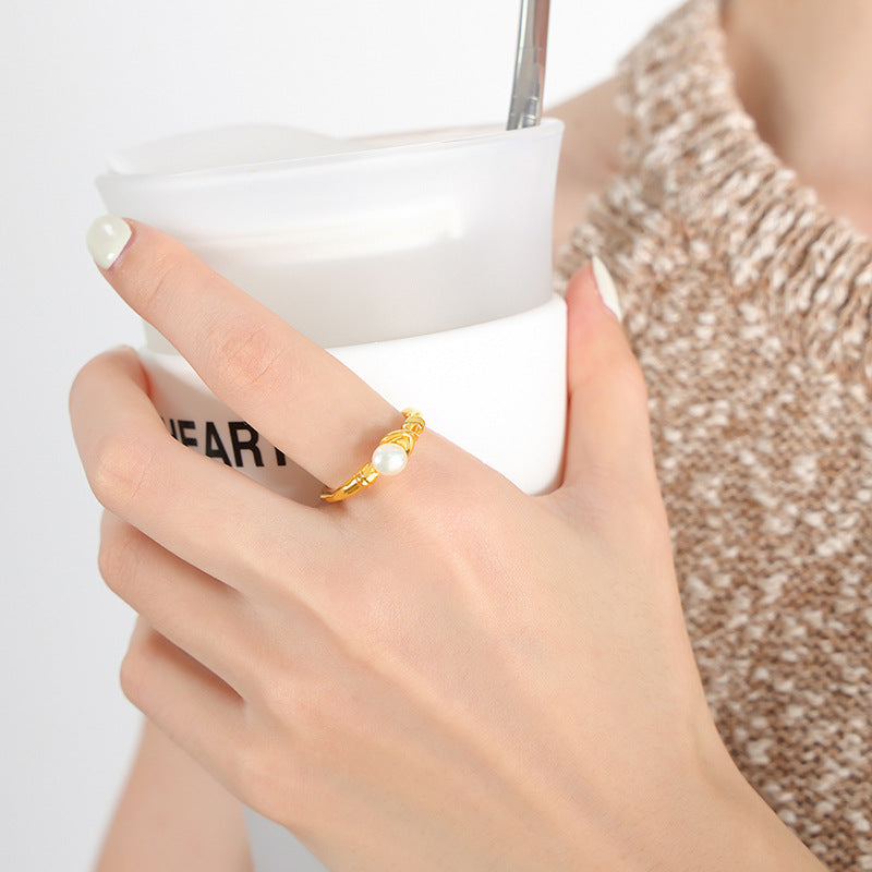 Hand wearing a gold ring with a pearl, holding a white cup.