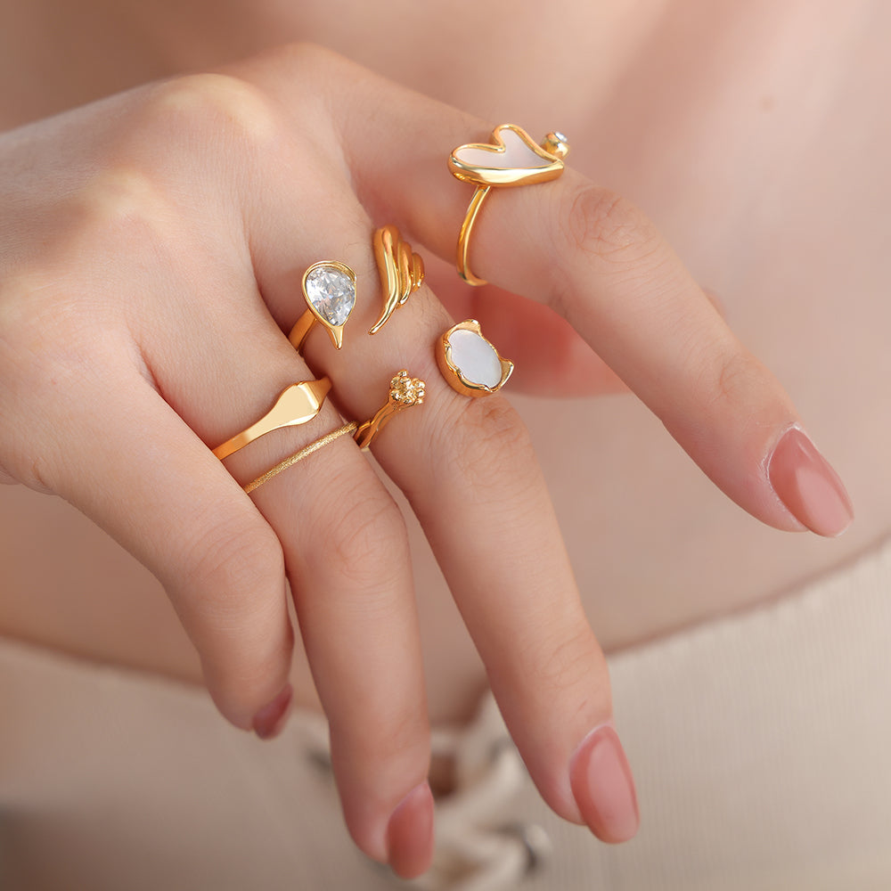Hand wearing multiple gold rings with gemstones on a neutral background
