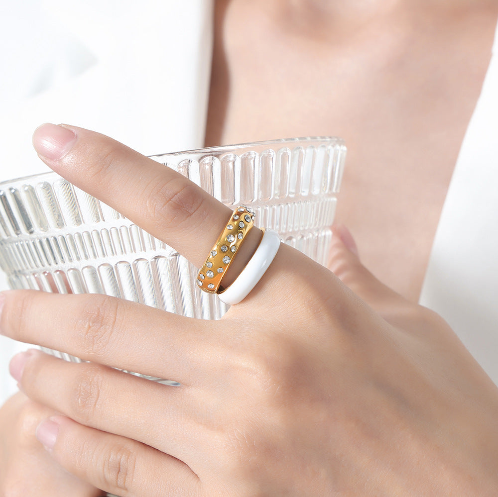 Hand wearing a gold ring with clear stones, holding a glass against a white background