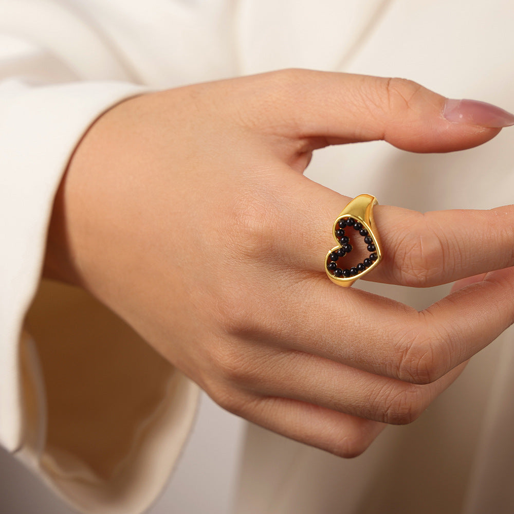 Hand wearing a gold ring with black gemstones on a neutral background
