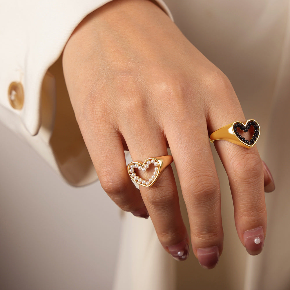 Hand wearing two gold heart-shaped rings on a neutral background