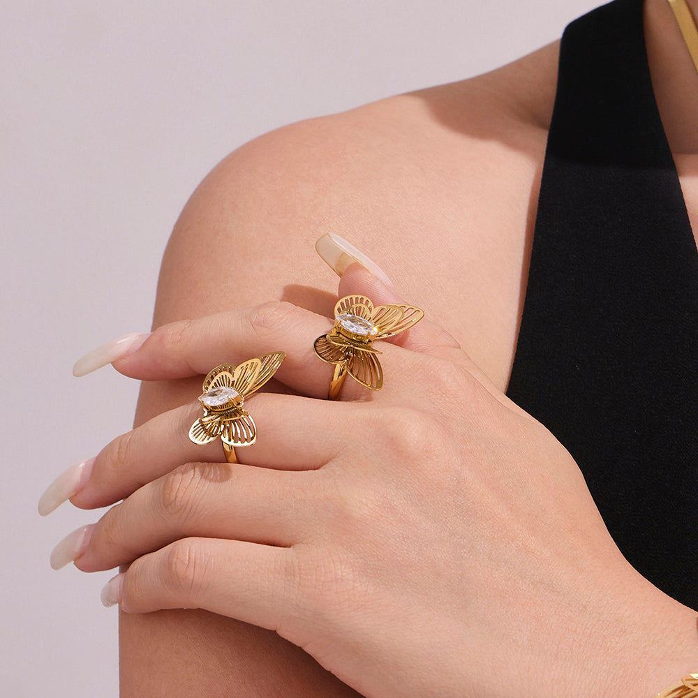 Gold butterfly rings on a hand against a light pink background