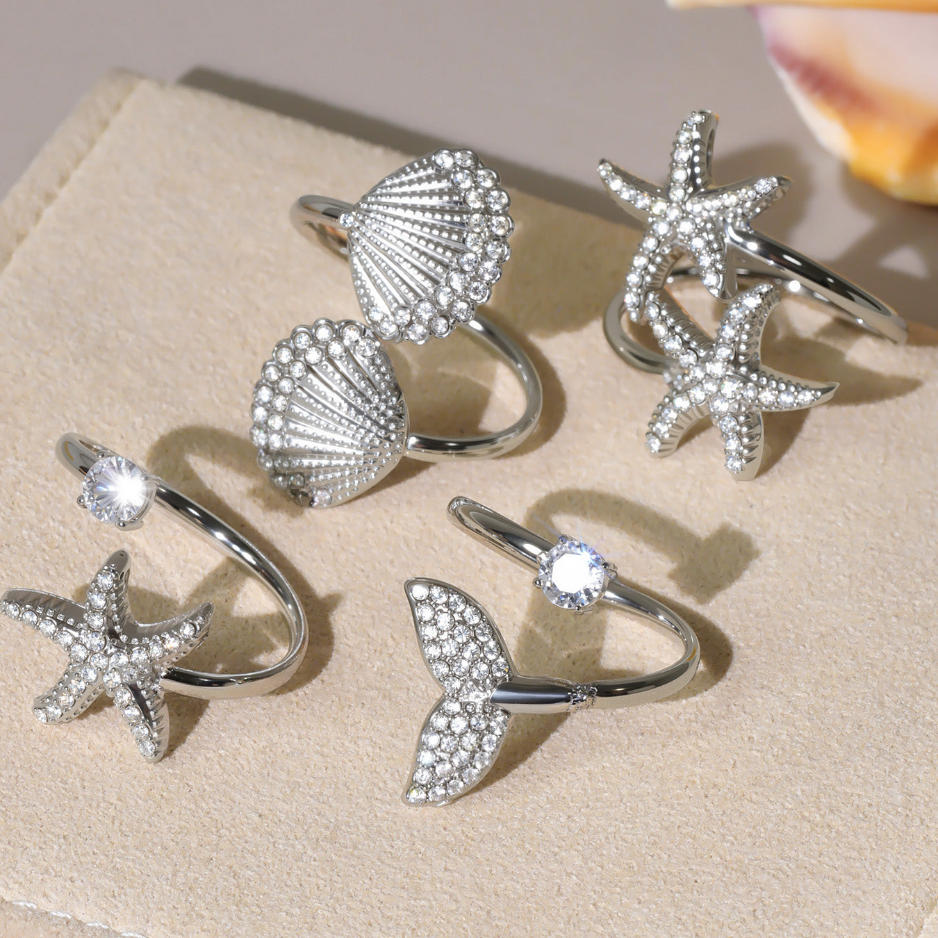 Silver ring with shell and starfish design on a beige surface