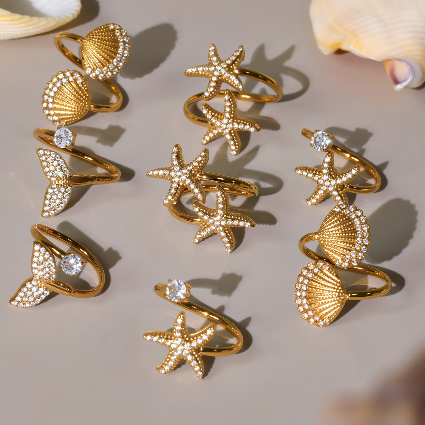 Gold rings with shell and starfish designs on a beige surface