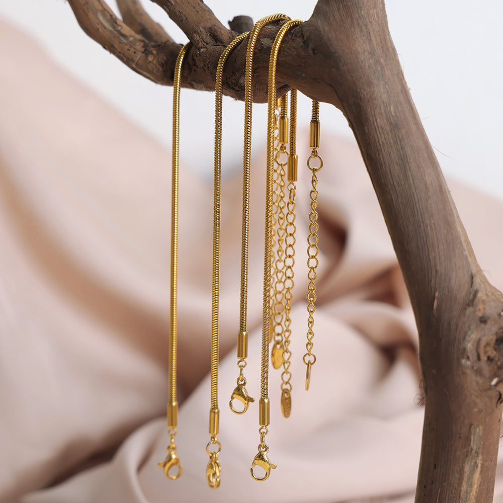 Gold necklaces of different lengths hanging on a branch with a soft background
