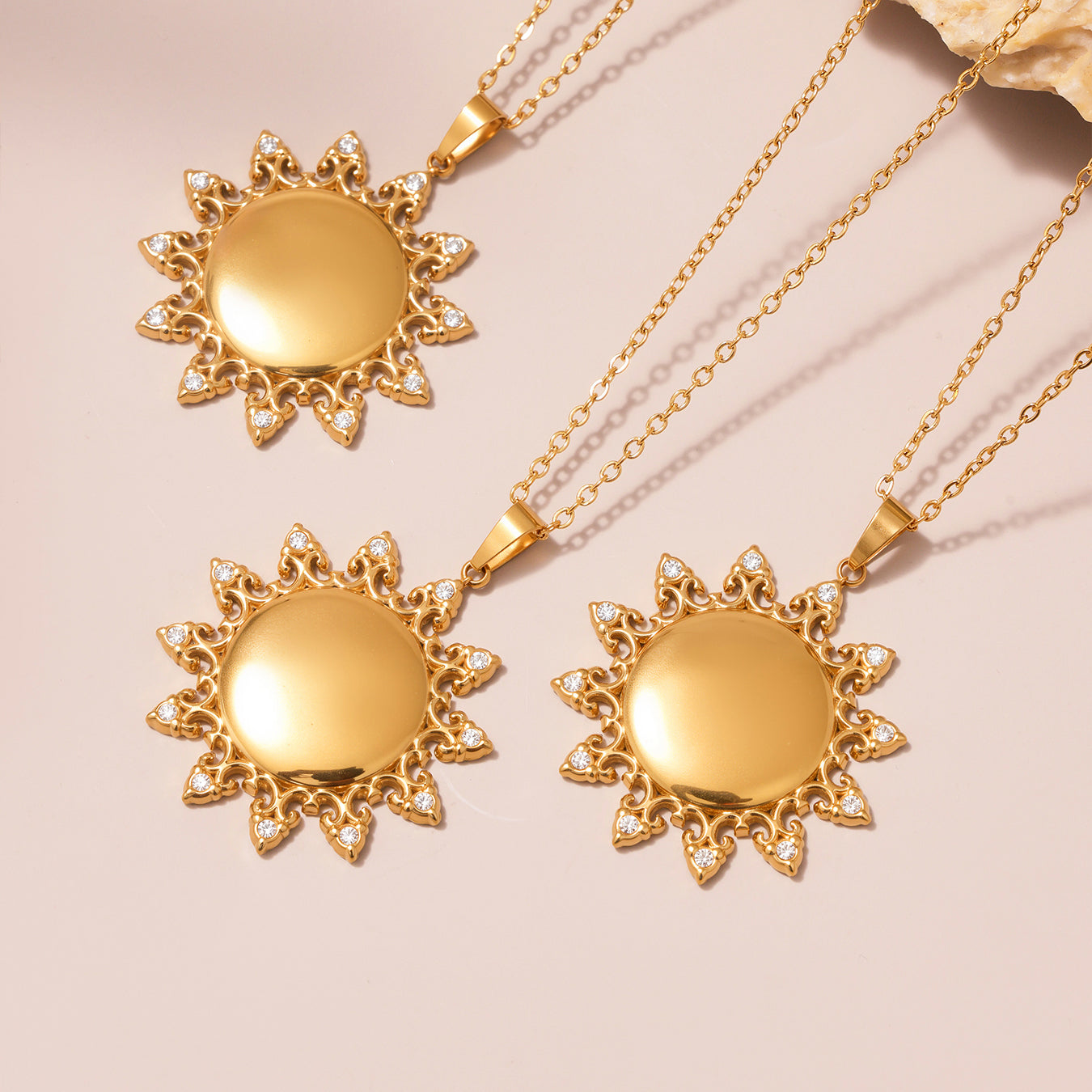Three gold sun-shaped pendants on gold chains against a beige background