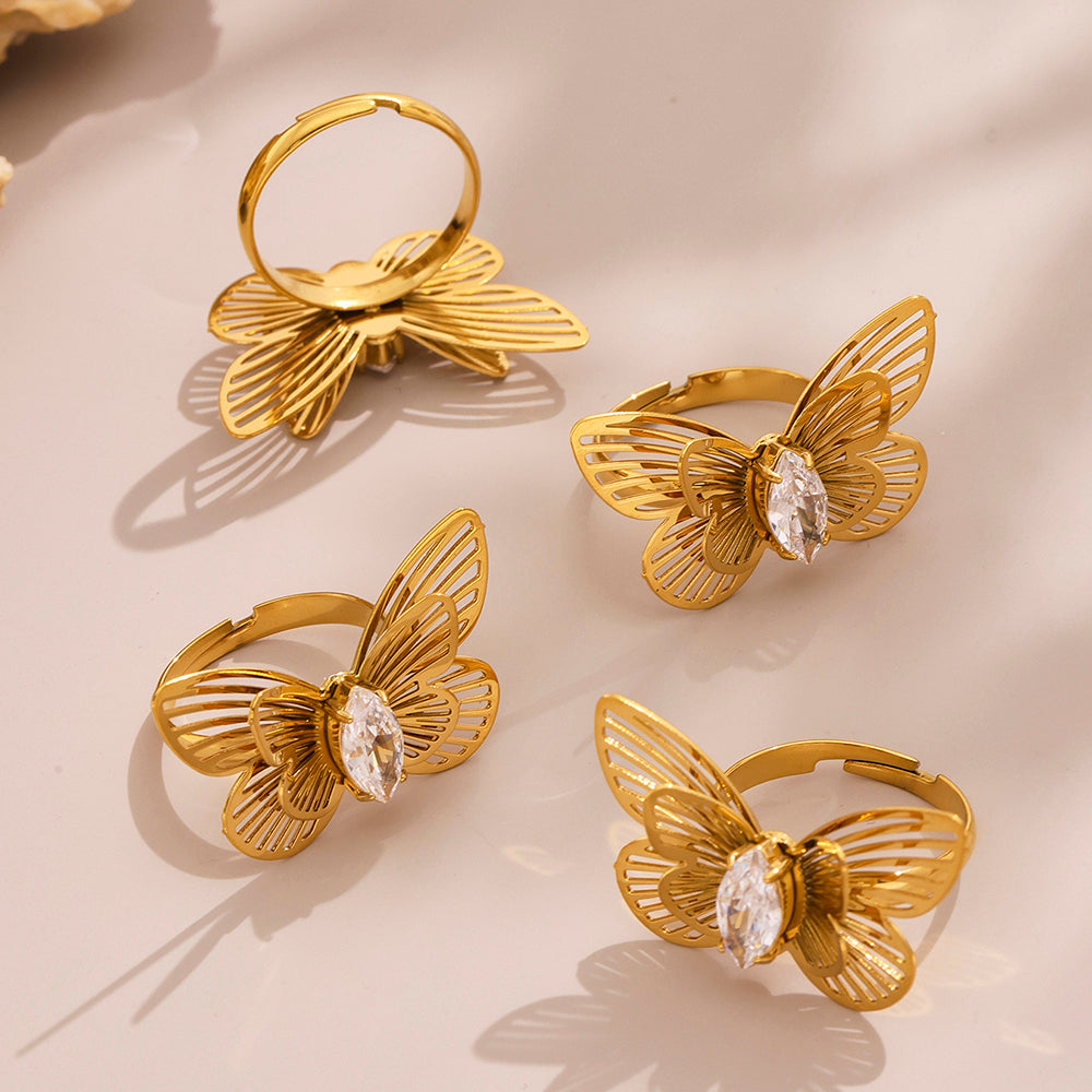 Gold butterfly-shaped rings with gemstones on a beige surface