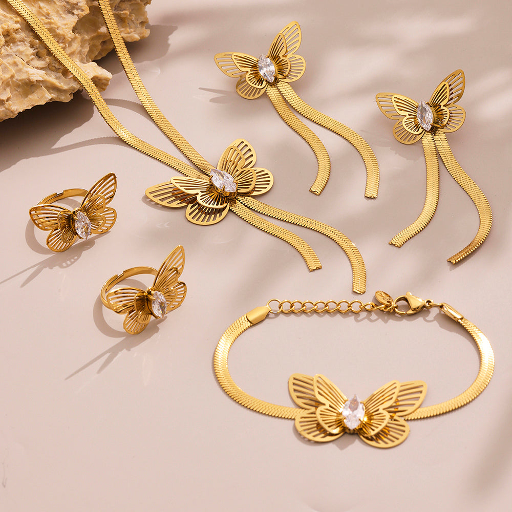 Gold butterfly-themed jewelry set including necklace, bracelet, and rings on a beige background.