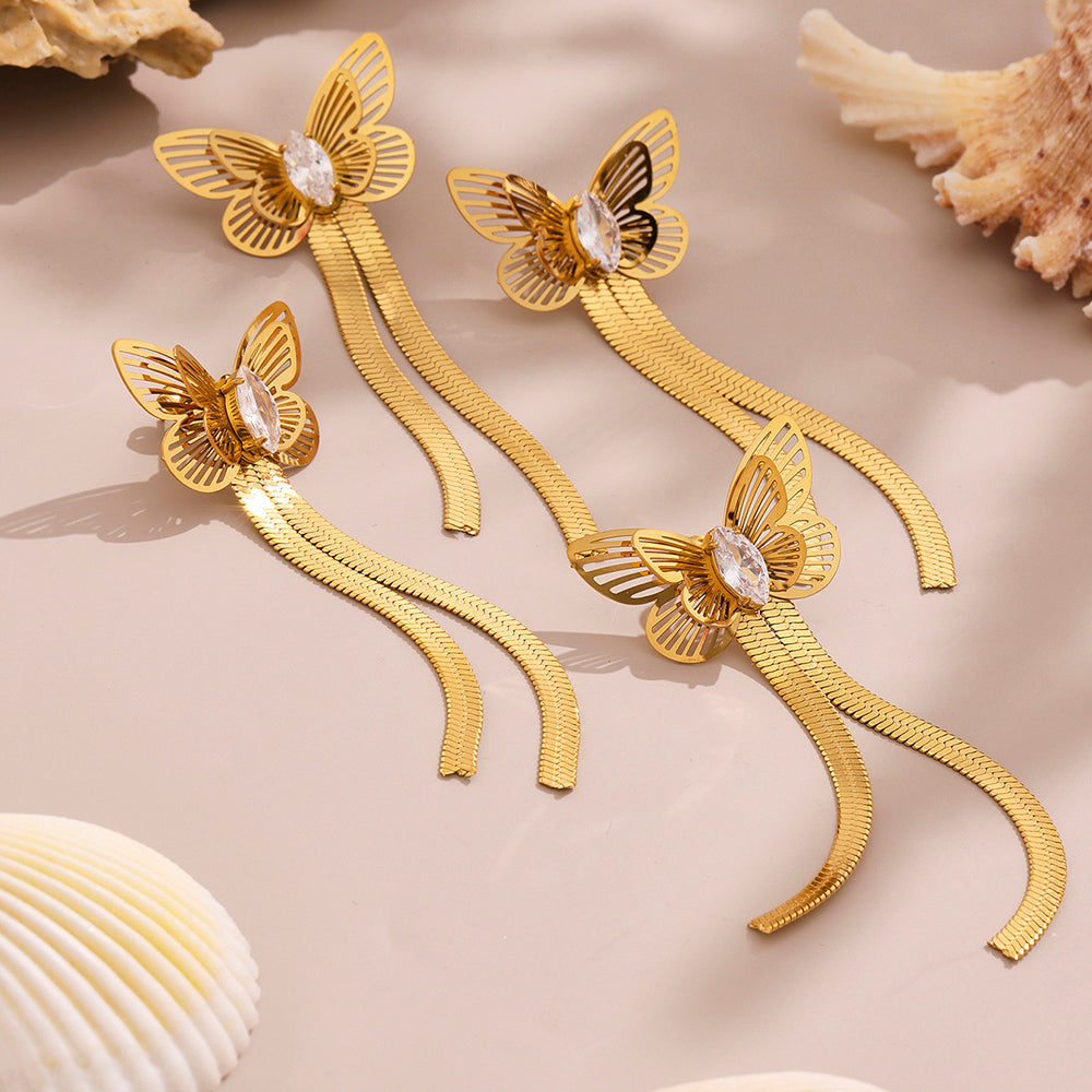 Gold butterfly earrings on a beige surface with shells in the background