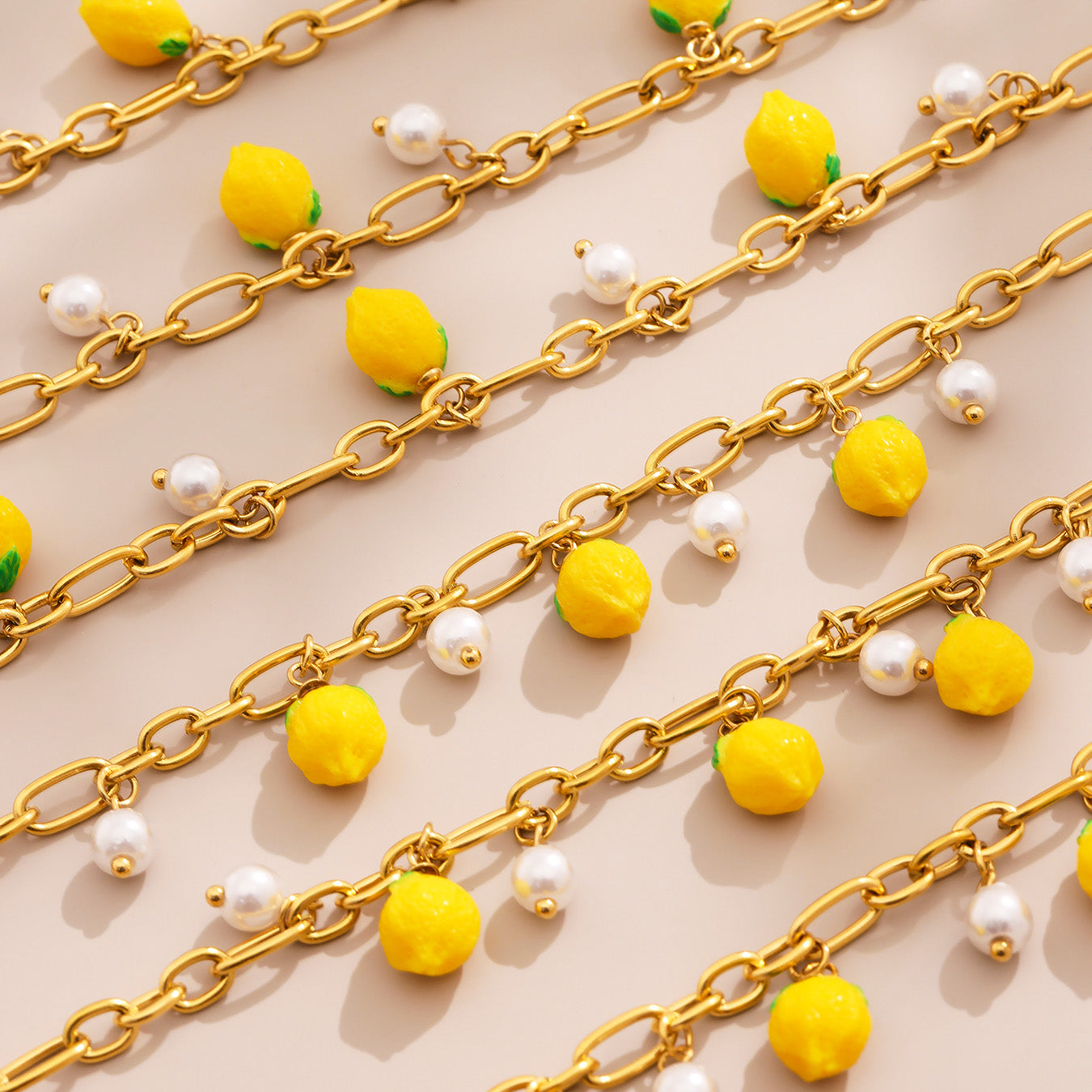 Gold chains with yellow lemon and white pearl pendants on a beige background