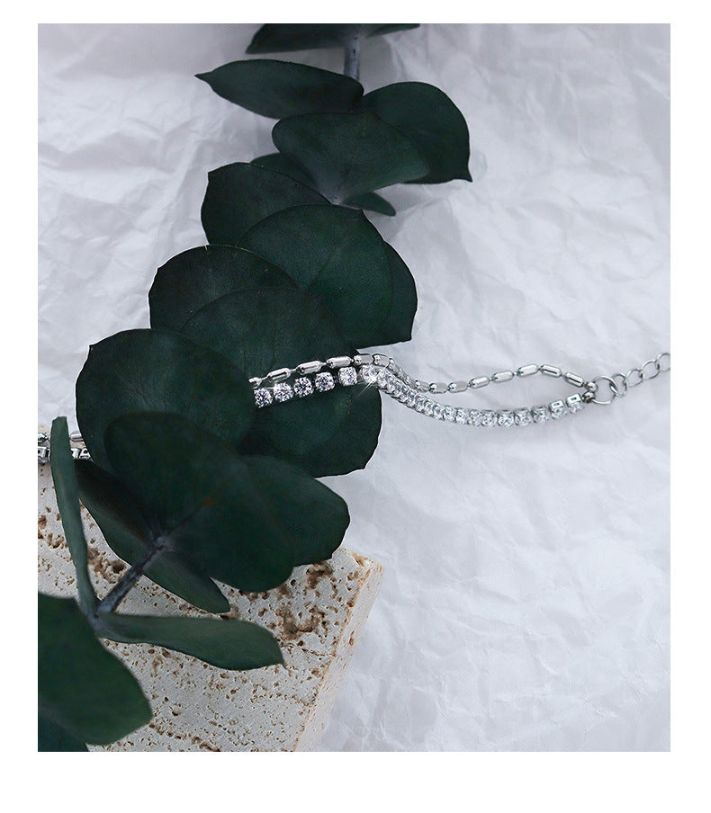 Silver necklace featuring diamond clasp displayed on green leaves – elegant jewelry photography