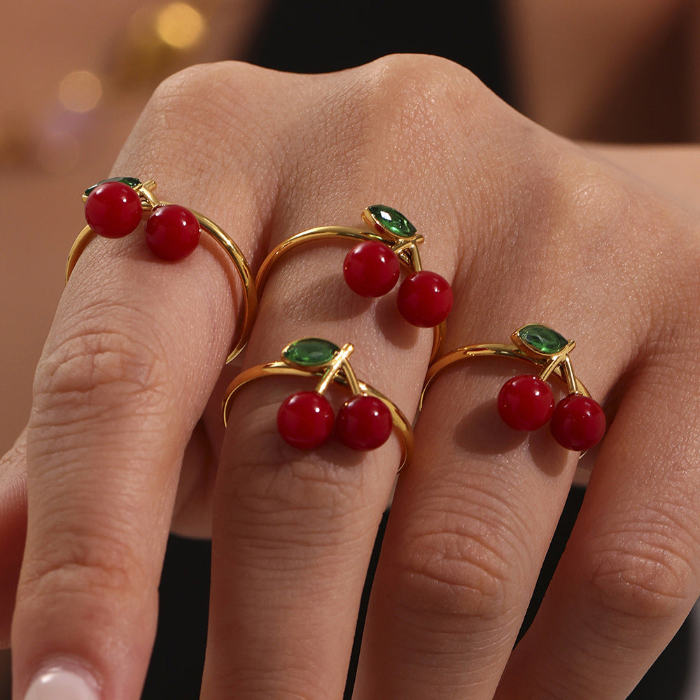 Hand wearing gold cherry sea glass rings with red berries and green leaf gemstones