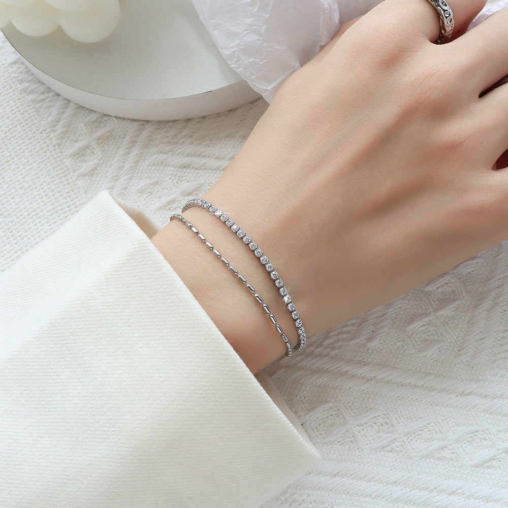 Close-up of hand wearing stacked silver bracelets on white fabric – modern layered stainless steel jewelry