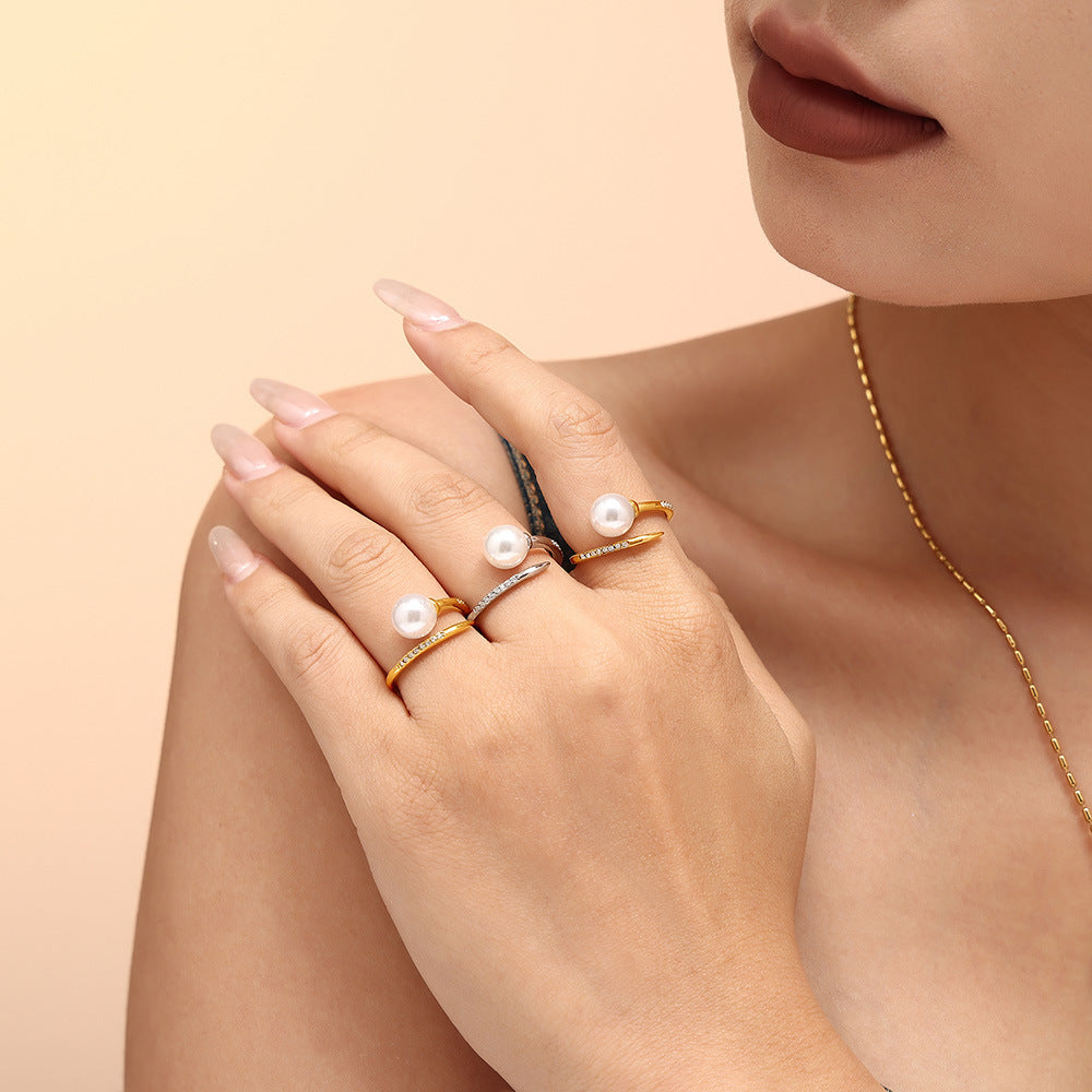 Woman’s hand wearing multiple gold pearl rings and a matching necklace on a beige backdrop