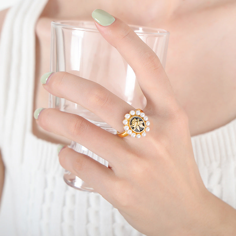 Hand wearing a bold gold baroque pearl ring with black center stone and sunflower design while holding a glass