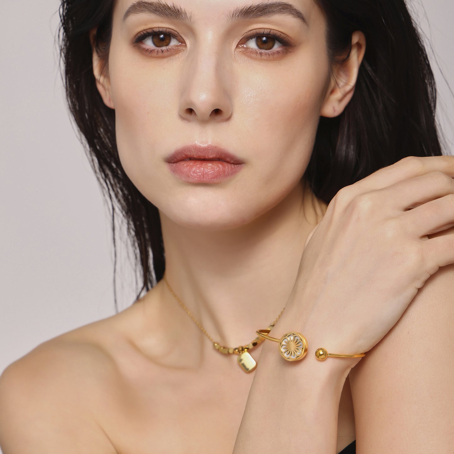 Woman showcasing gold necklace and matching bracelet on plain neutral background