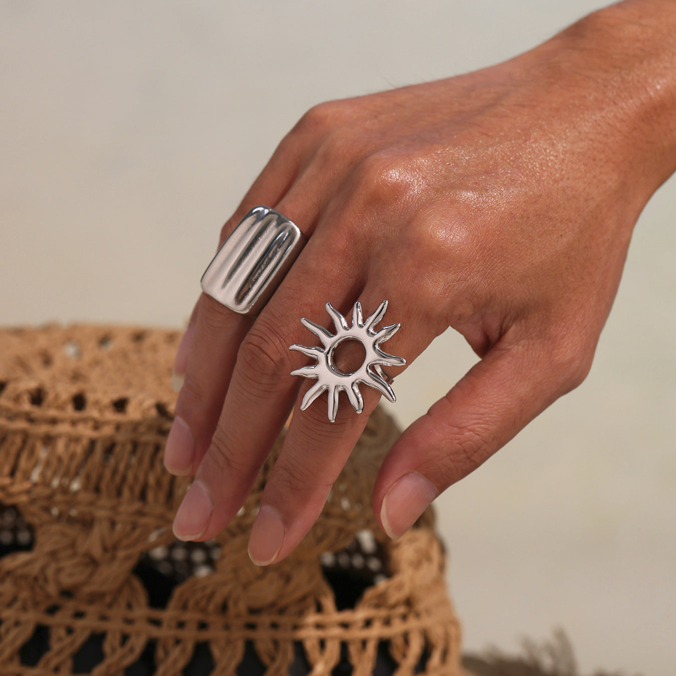 Hand wearing two silver chunky rings on each finger, neutral background.