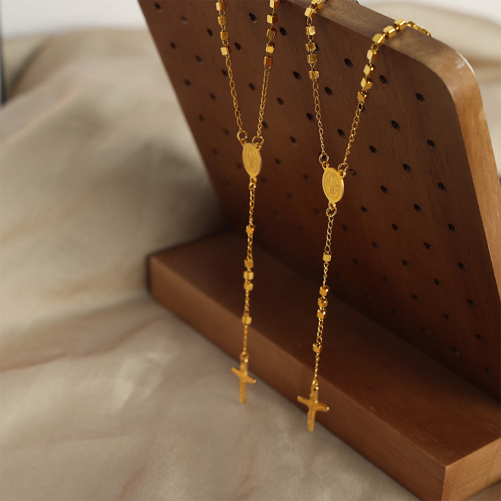 Long Gold Cross Pendant Necklace Resting on White Plate with Soft Lighting
