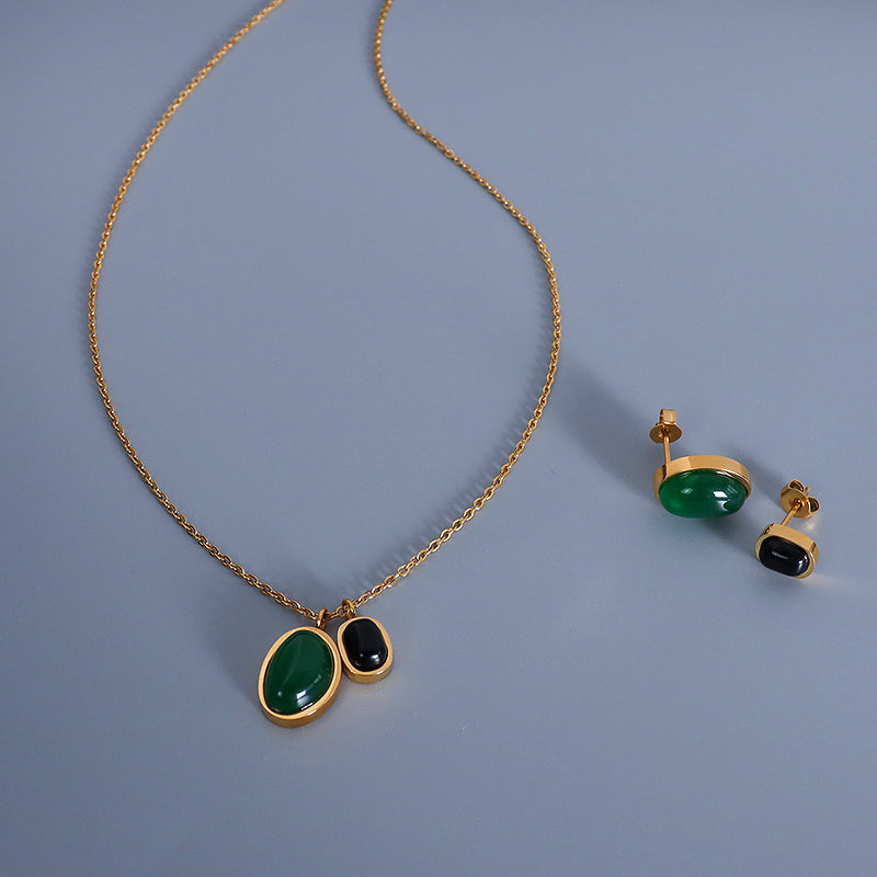 Gold necklace with green and black stones on a blue background