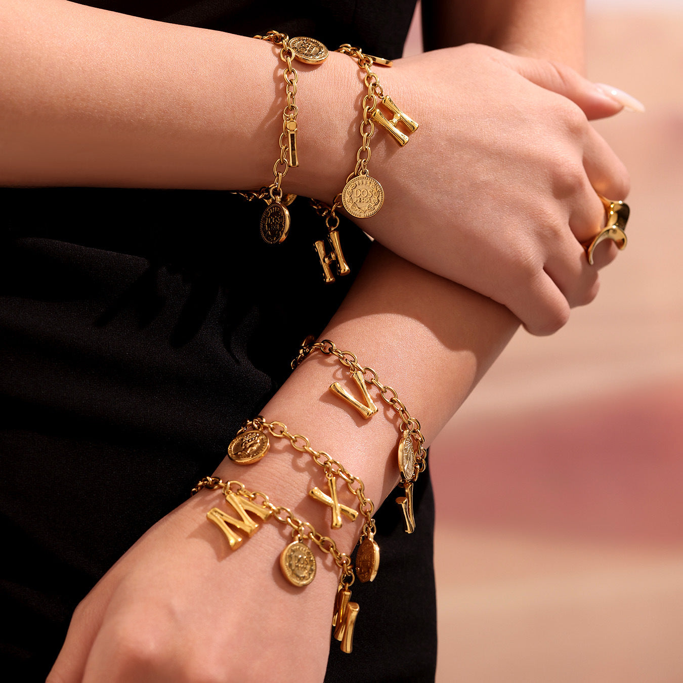 Gold bracelets with various charms on a person's wrist against a blurred background