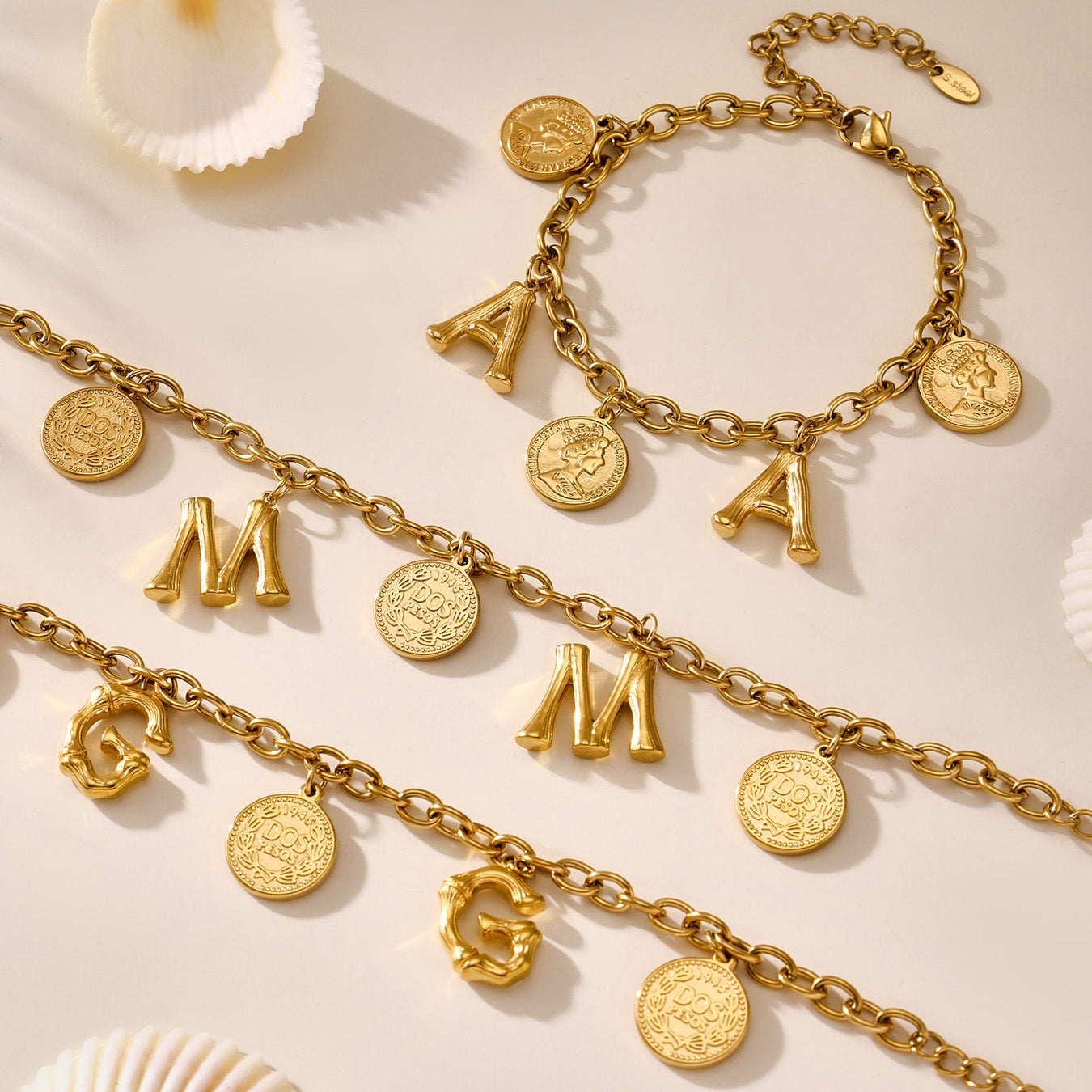 Gold bracelets with letter and coin charms on a beige background