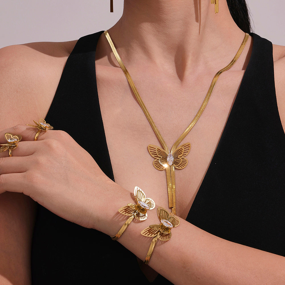 Gold butterfly-themed jewelry set including necklace, bracelet, and rings on a model wearing a black dress.
