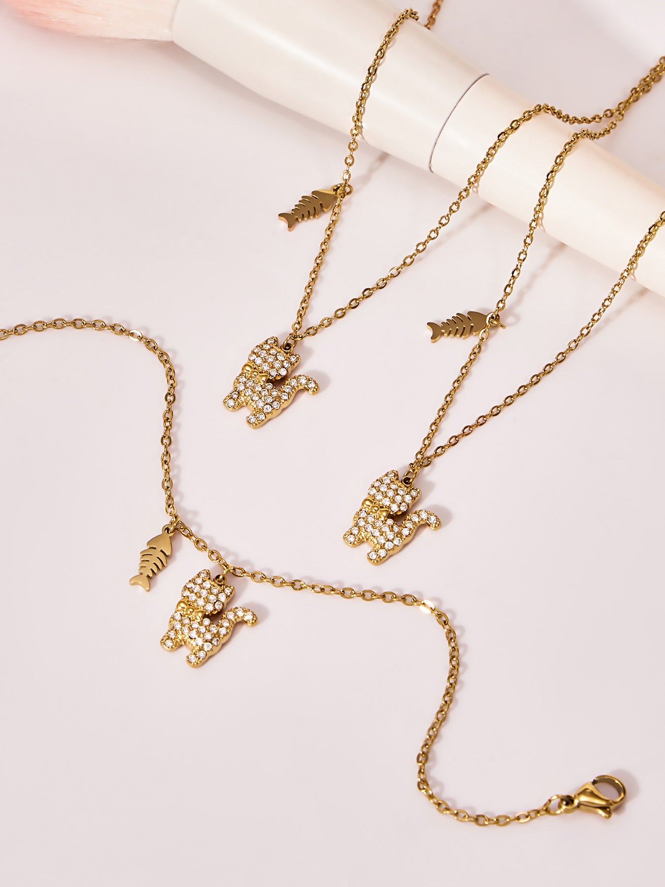 Flat lay of the gold cat necklace showing the stainless steel chain, CZ cat pendant, and paired fishbone charm.