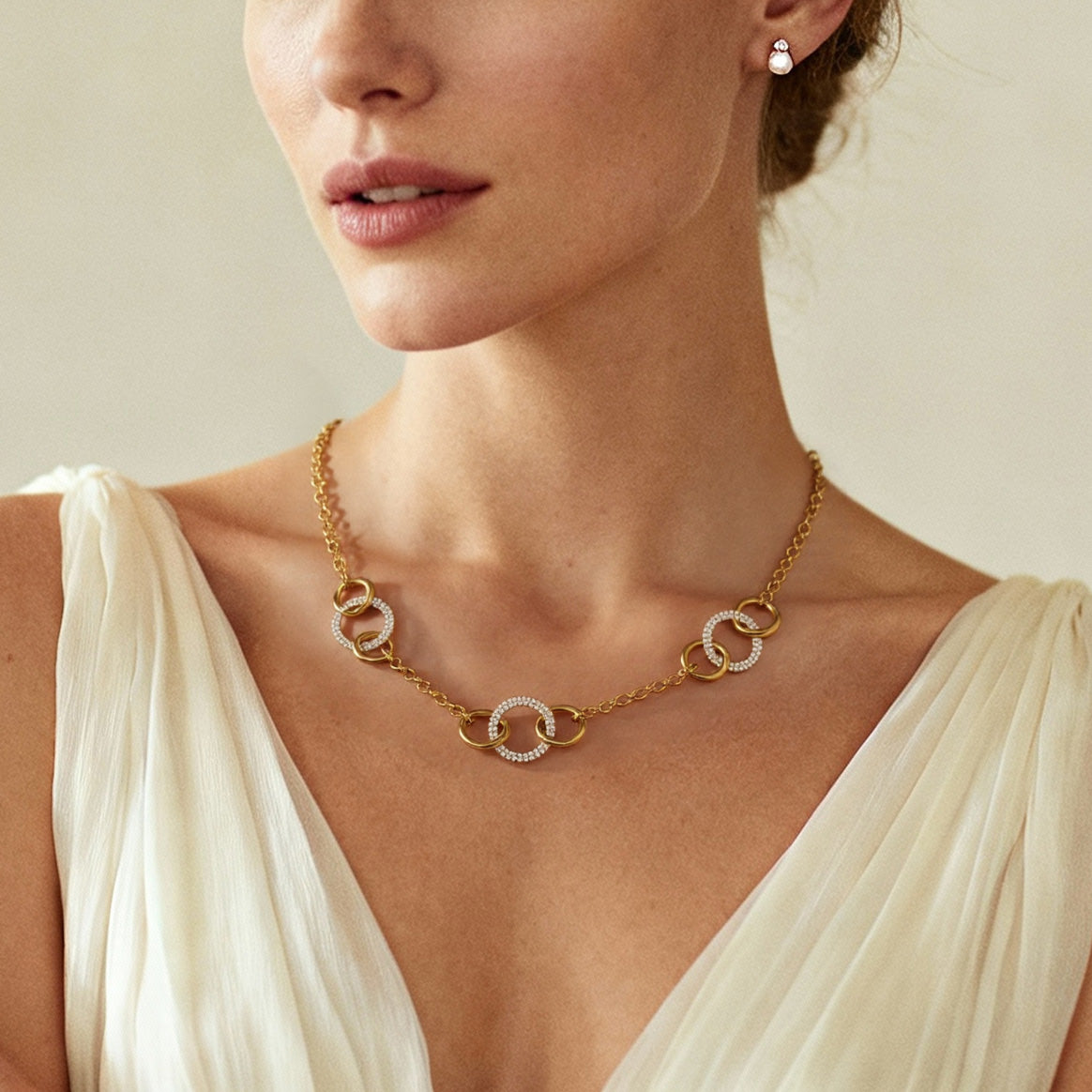 Close-up of interlocking gold circle necklace with diamond accents styled with minimal cream dress